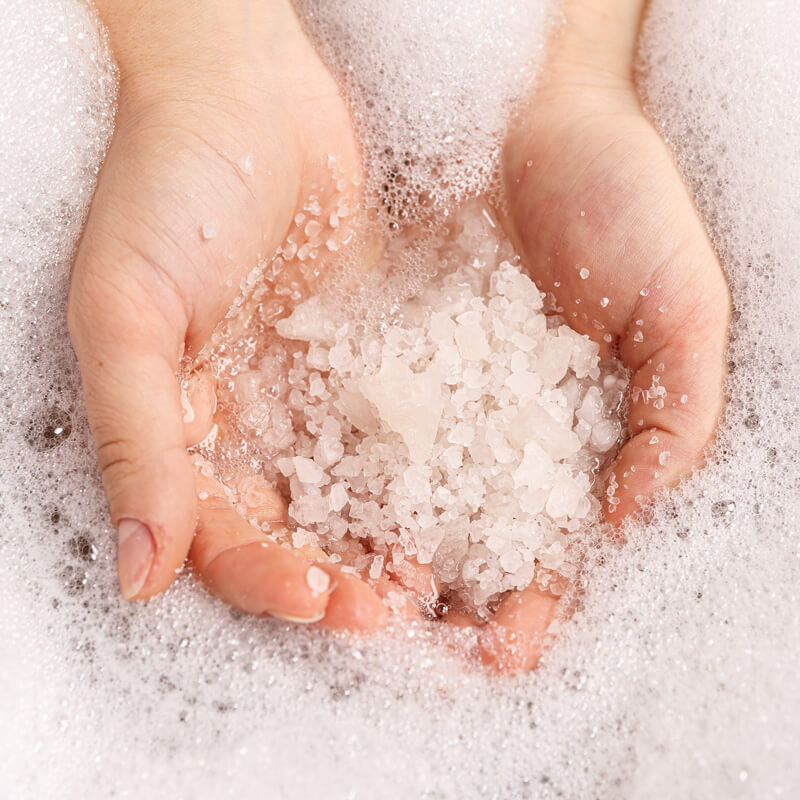 Mani immerse in acqua con sali da bagno, espressione della cura e sostenibilità della cosmetica solida.