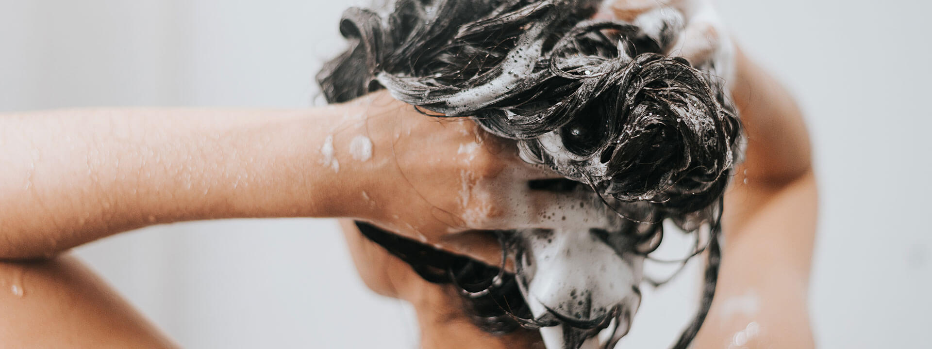 Uomo che si lava i capelli con abbondante schiuma, simbolo della qualità nei prodotti per capelli conto terzi, disponibili da piccoli lotti a grandi quantità.