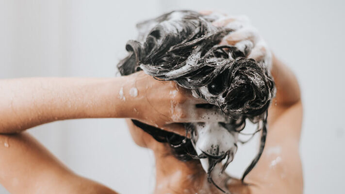 Una donna che si lava i capelli durante la routine di haricare, rappresentando la produzione conto terzi per piccoli lotti e grandi quantità.