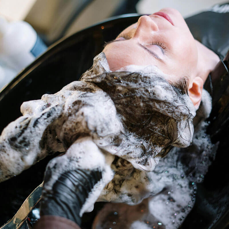 Parrucchieri lavano i capelli lunghi di una cliente con tanta schiuma, utilizzando prodotti realizzati conto terzi per parrucchieri.